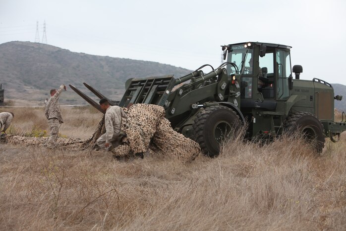 Marines use a forklift to lift camouflage netting over a tent  during 9th Communication Battalion’s field exercise at Camp Pendleton, Sept. 15. During the exercise Marines constructed and operated from tents. The exercise was designed to prepare the Marines for their upcoming deployment.