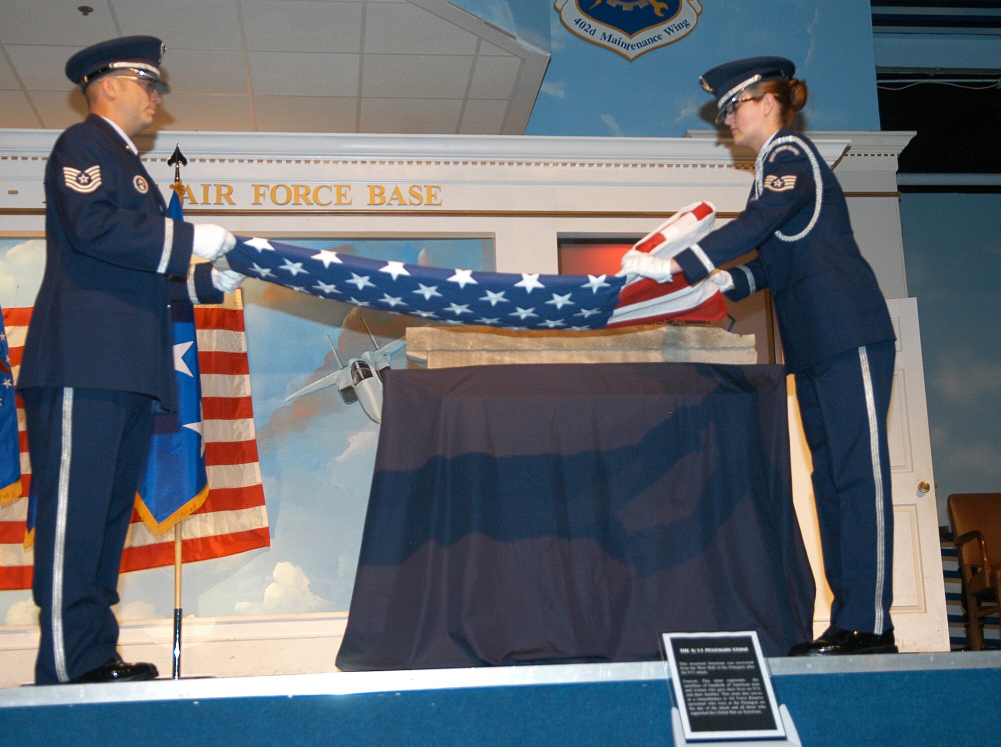 Tech. Sgt. John Besselman and Staff Sgt. Kelly Salinas, Robins Honor Guards, remove and fold an American  flag which was draped over a fragment from the west wall of the Pentagon. U. S. Air Force photo by Sue Sapp