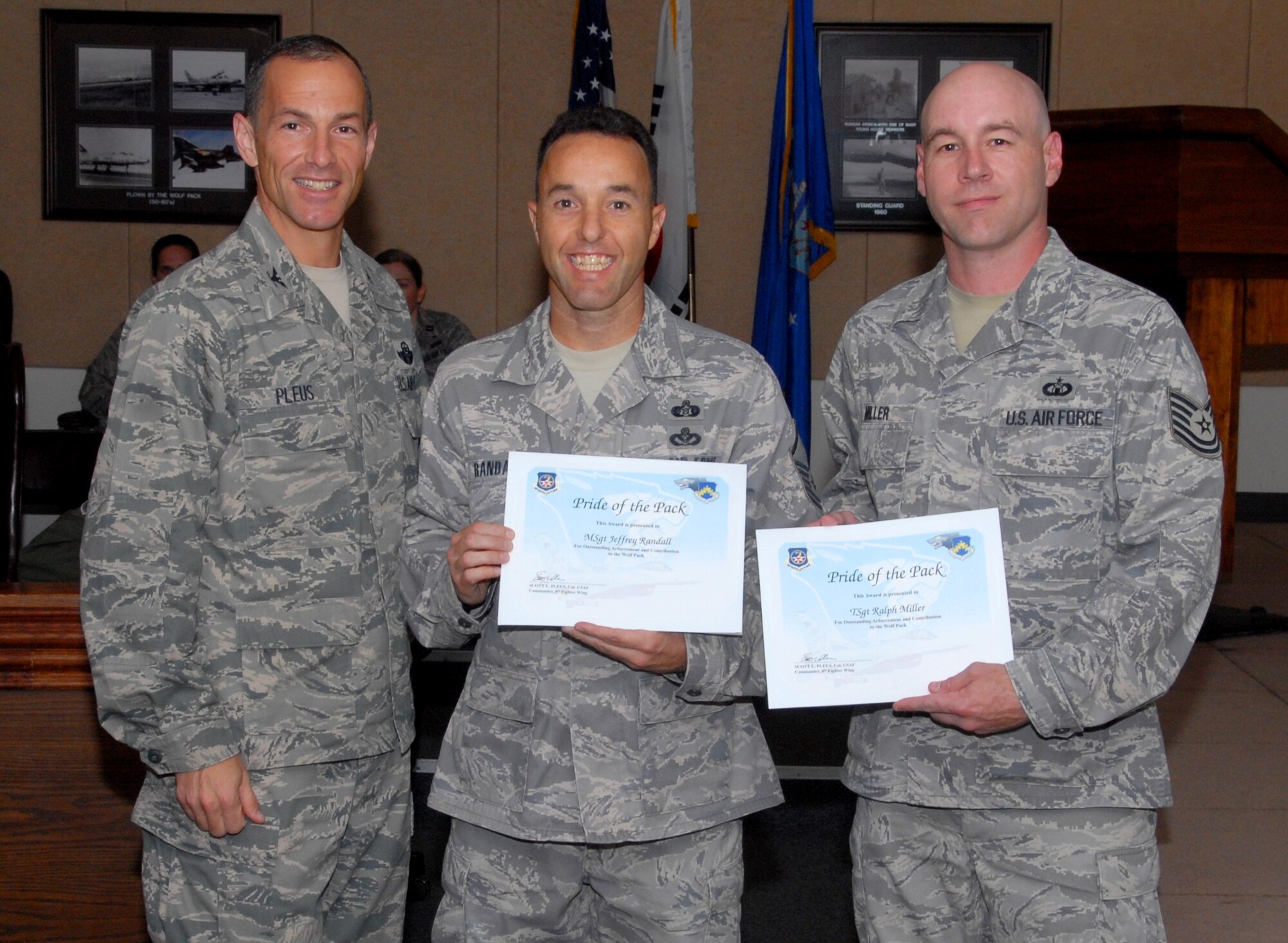 KUNSAN AIR BASE, Republic of Korea -- Col. Scott Pleus, 8th Fighter Wing commander, presents the Pride of the Pack award to Master Sgt. Jeff Randall, 8th Civil Engineer Squadron readiness and emergency management superintendent, and Tech. Sgt. Ralph P. Miller Jr., 8th Operations Support Squadron air traffic control watch supervisor, here Sept. 15. (U.S. Air Force photo/1st Lt. Trisha Eldredge)