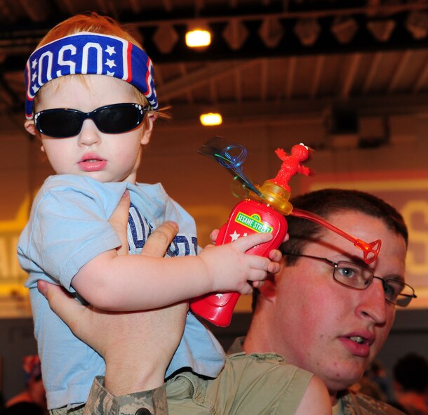 RAF MILDENHALL, England -- Adrian Struthers, 2, son of Senior Airman Thomas Struthers, 100th Logistics Readiness Squadron, sits on his dad's shoulders as he shows off his bandana and his Elmo novelty souvenir after watching the Sesame Street/United Services Organization Experience for Military Families show at the North Side Fitness Center, Sept. 15, 2011. More than 1,000 people attended the two show performances. (U.S. Air Force photo by Karen Abeyasekere)