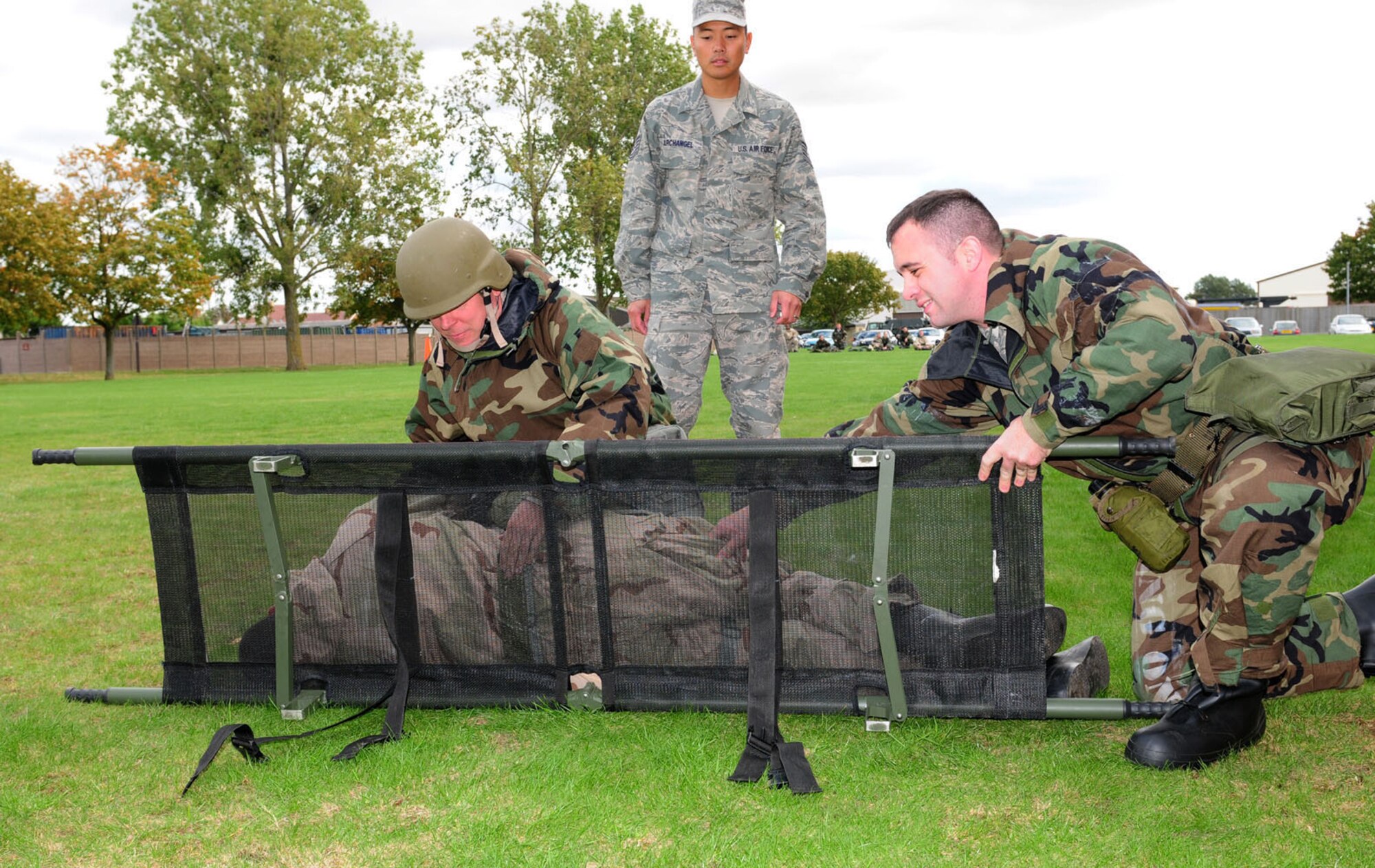 RAF MILDENHALL, England -- Two members from RAF Mildenhall carefully roll Staff Sgt. Edy Cruz-Xuarez, 100th Civil Engineer Squadron, onto a fold-up litter as instructor, Tech. Sgt. Joseph Archangel, 488th Intelligence Squadron Medical Element, looks on during the self-aid and buddy care portion of an ATSO rodeo Sept. 14, 2011. In addition to SABC, participants wore different stages of MOPP gear, and went through various areas of training: post attack reconnaissance, contamination control station, ATSO familiarization and weapons familiarization. (U.S. Air Force photo by Karen Abeyasekere)