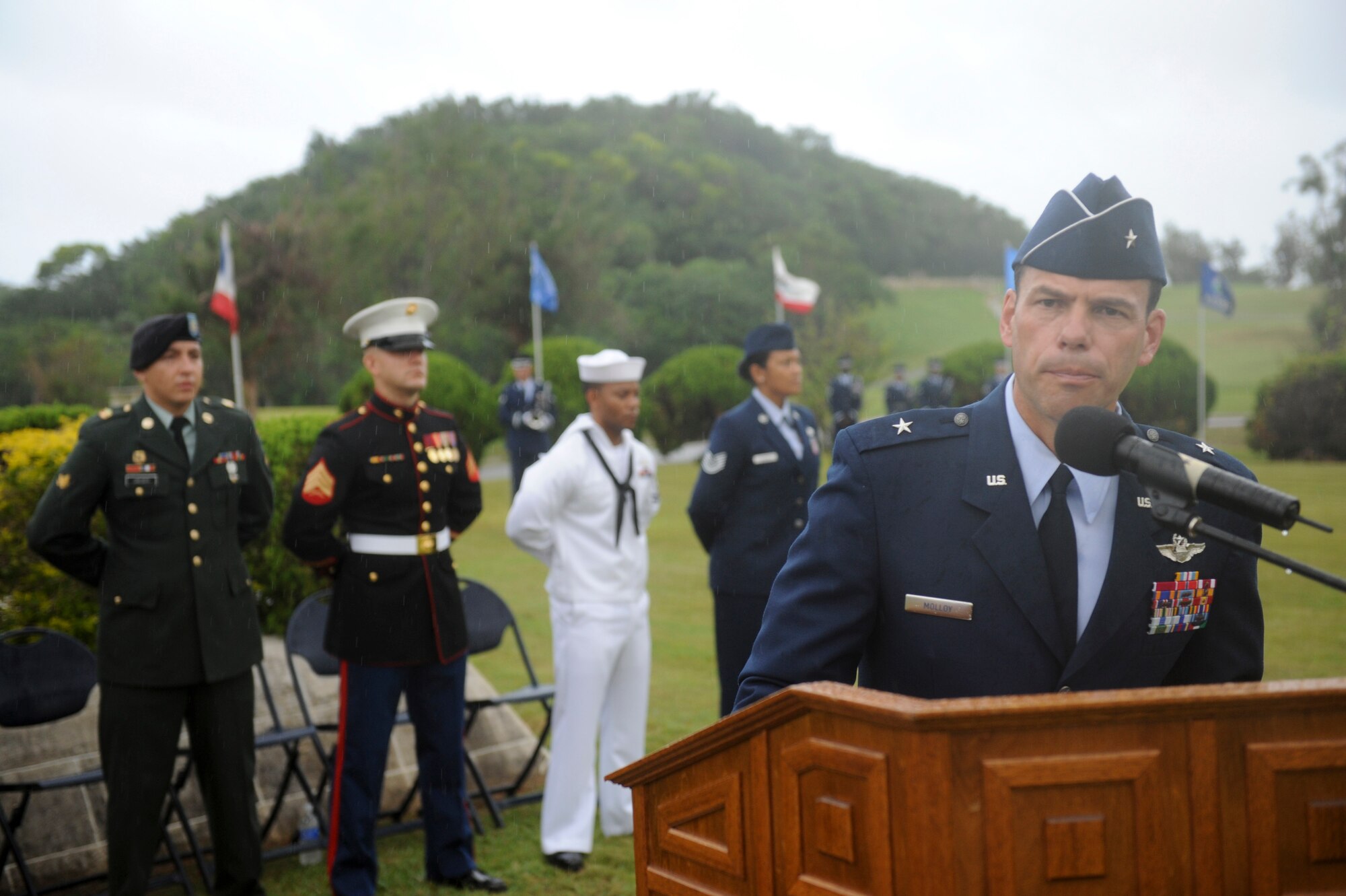 Brig. Gen. Matthew Molloy, 18th Wing commander, speaks in the rain as representatives from all four branches of service look on during Kadena's Prisoner of War and Missing in Action ceremony Sept. 16, 2011. The national POW/MIA recognition day is observed on the third Friday of September every year, but it is important to always remember the sacrifice of prisoners of war and those missing in action.  (U.S. Air Force photo by Airman 1st Class Brooke P. Beers)     