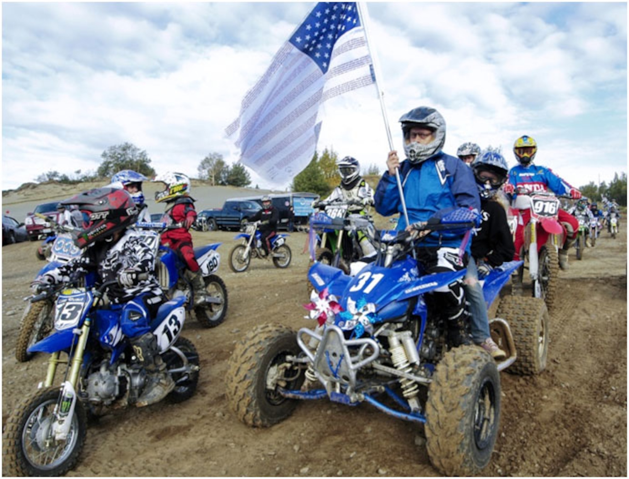Anchorage -- Airport Police and Fire Officer, Mike Oden, holds the Flag of Heroes as riders line up for the ceremonial lap prior to the start of the races at the Jodhpur Motocross Track., The flag is inscribed with the names of the fallen emergency responders of the September 11th, 2001 attacks. (U.S. Air Force photo/Percy Jones)