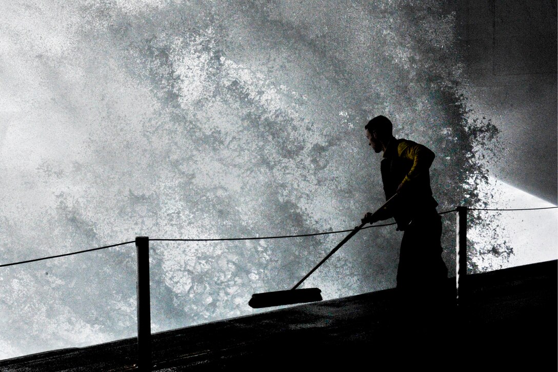 U.S. Navy Petty Officer 3rd Class Travis Bloomer attempts to sweep water out of the hangar bay onboard the aircraft carrier USS John C. Stennis during a replenishment at sea mission in the Indian Ocean, Sept. 11, 2011. Bloomer is an aviation boatswain's mate.
