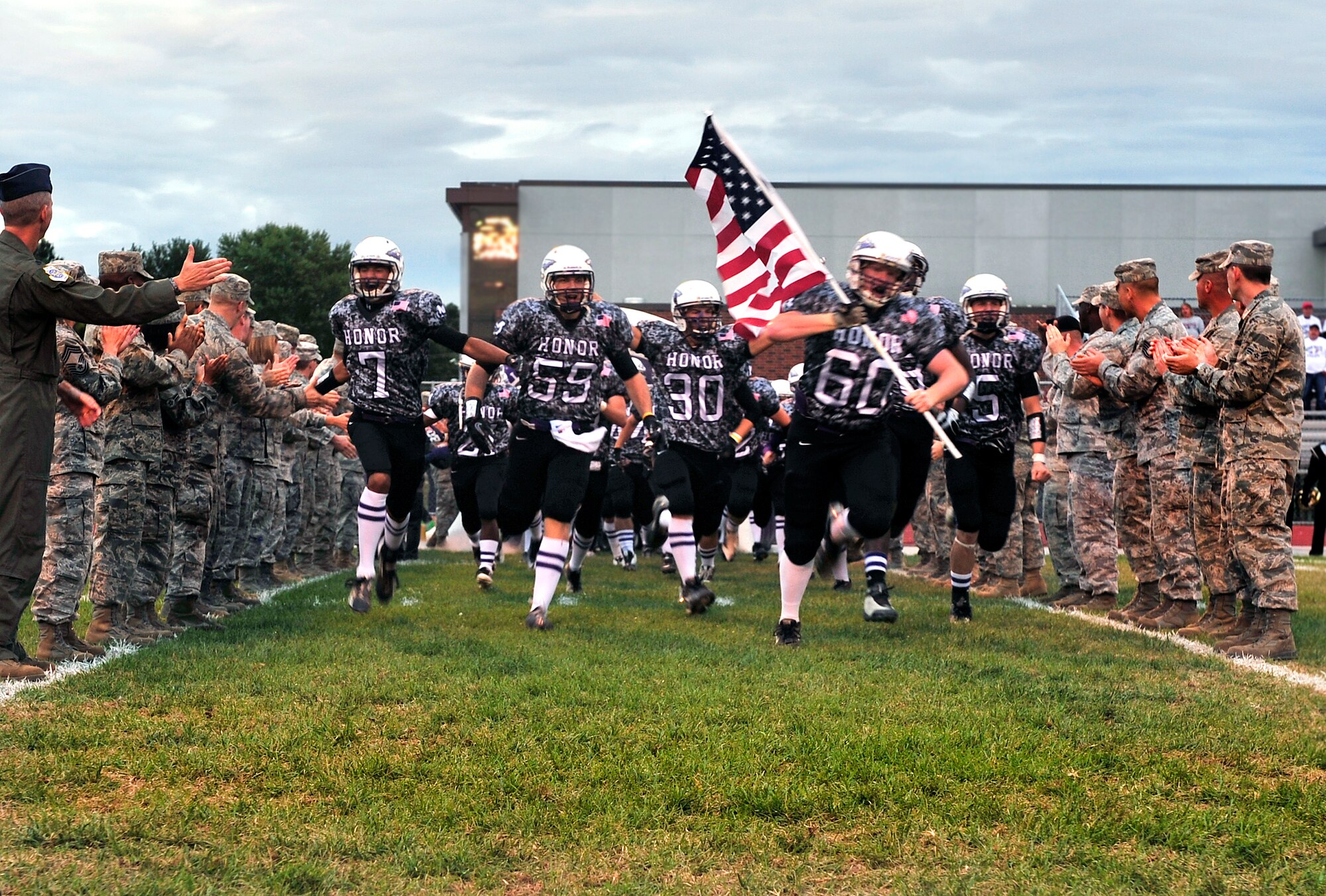 The Mascoutah Indians carry the American flag through Team Scott representatives during the pregame ceremony at the inaugural Annual Armed Forces Football Classic Sept. 16, 2011 at Mascoutah High School Stadium. Mascoutah beat Highland 34 – 18, their first win against their rival in 5 years.( U.S. Air Force photo/ Staff Sgt. Stephenie Wade)