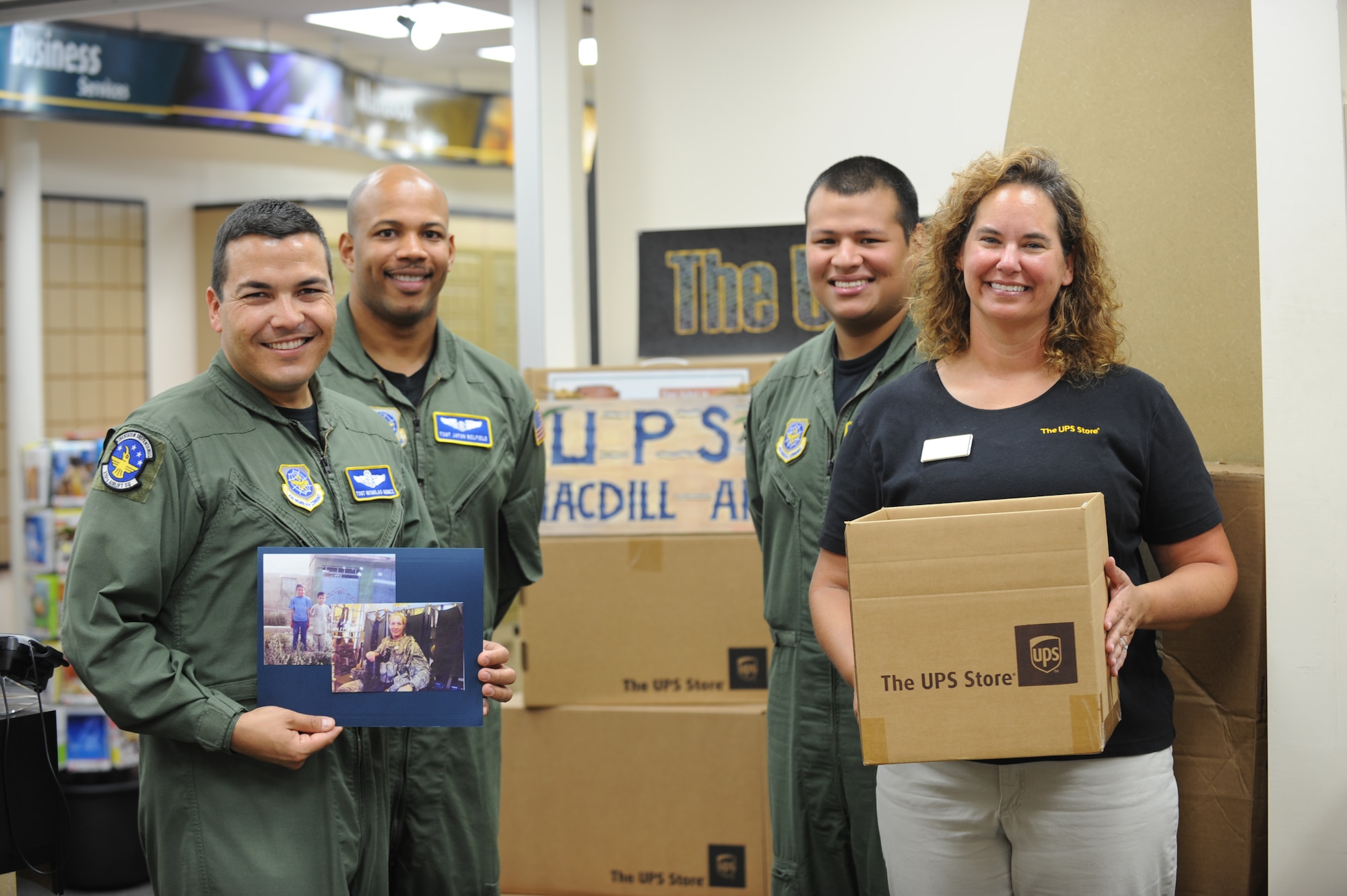 Tech. Sgt. Nicholas Gomez, Tech. Sgt. Jaton Belfield and Staff Sgt. Kevin Sanchez of the 310 Airlift Squadron, and Regina Pugh the MacDill UPS store owner, pose with photos of forward deployed Operation Outreach volunteer Capt. Donna Besley and some Afghan children in front of boxes of donated clothes at MacDill AFB, Fla. Sept.  12, 2011. Members from the 310th Airlift Squadron at MacDill Air Force Base collected more than 150 pounds of clothing and Ms. Pugh graciously donated the boxes and covered the cost of shipment. (US Air Force photo by Tech Sgt. Tanika Belfield /Released)