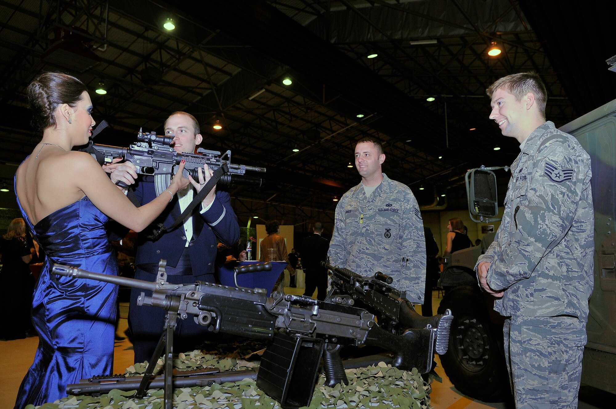 ROYAL AIR FORCE LAKENHEATH, England - 1st Lt. Jonathan Cates, 48th Medical Support Squadron patient administration chief, helps his wife Chiara Cates hold an M-4 machine gun at the Security Forces demonstration table during the Air Force Ball in Hangar 7 on Sept. 17, 2011.  More than 600 people attended the event, which highlighted the different decades and the history of RAFs Lakenheath and Mildenhall.  (U.S. Air Force photo by Staff Sgt. Connor Estes)