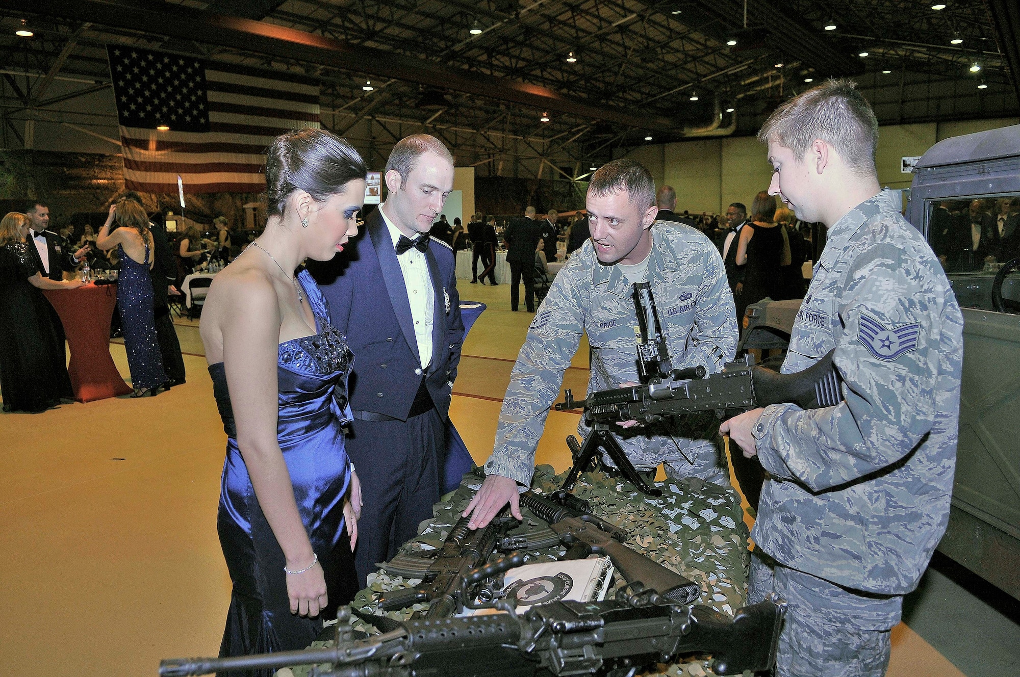 ROYAL AIR FORCE LAKENHEATH, England - Staff Sgt. Lawrence Price, 48th Security Forces armory NCO in charge (middle), explains the different weapons at the 48th SFS demonstration table during the Air Force Ball in Hangar 7 on Sept. 17, 2011.  More than 600 people attended the event, which highlighted the different decades and the history of RAFs Lakenheath and Mildenhall.  (U.S. Air Force photo by Staff Sgt. Connor Estes)es)