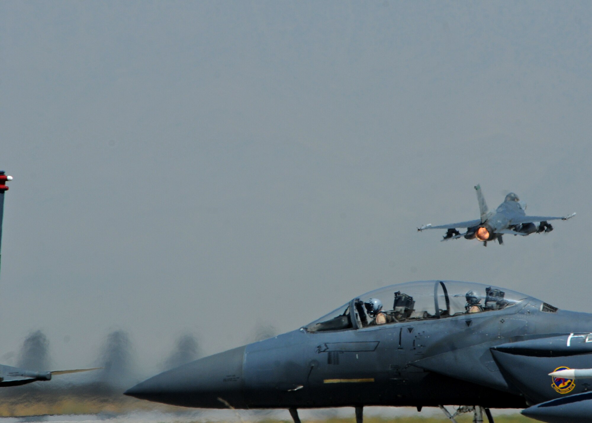 BAGRAM AIRFIELD, Afghanistan -- An F-16 Fighting Falcon from the 555th Expeditionary Fighter Squadron takes off as two F-15E Strike Eagles from the 389 EFS taxi out to the runway here Sep. 20 2011. The F-16 is a compact, multi-role fighter aircraft. It is highly maneuverable and has proven itself in air-to-air combat and air-to-surface attack. The F-15 is a dual-role fighter designed to perform air-to-air and air-to-ground missions. It can penetrate enemy defense and outperform and outfight any current enemy aircraft. (U.S. Air Force photo/ Senior Airman Krista Rose)