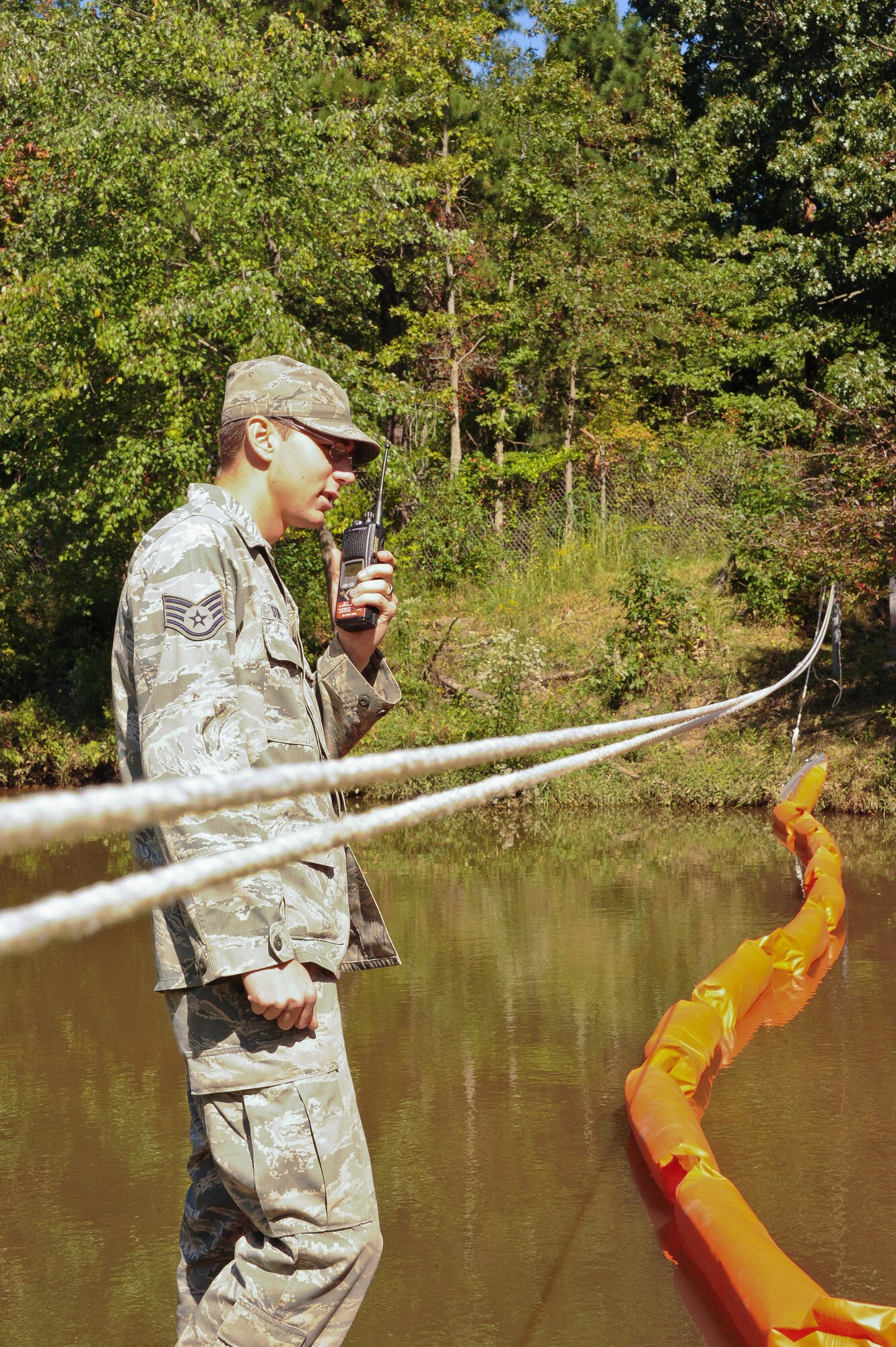 Staff Sgt. Jordan Stipcak, JB MDL Emergency Management trainer, radios to emergency management supervisors that a barrier stretched across a stream is installed properly, during a fuel spill exercise Sept. 16. The barrier was stretched across a stream to collect any fuel that may have spilled into it. (U.S. Air Force photo by Airman 1st Class Dennis Sloan/Released)