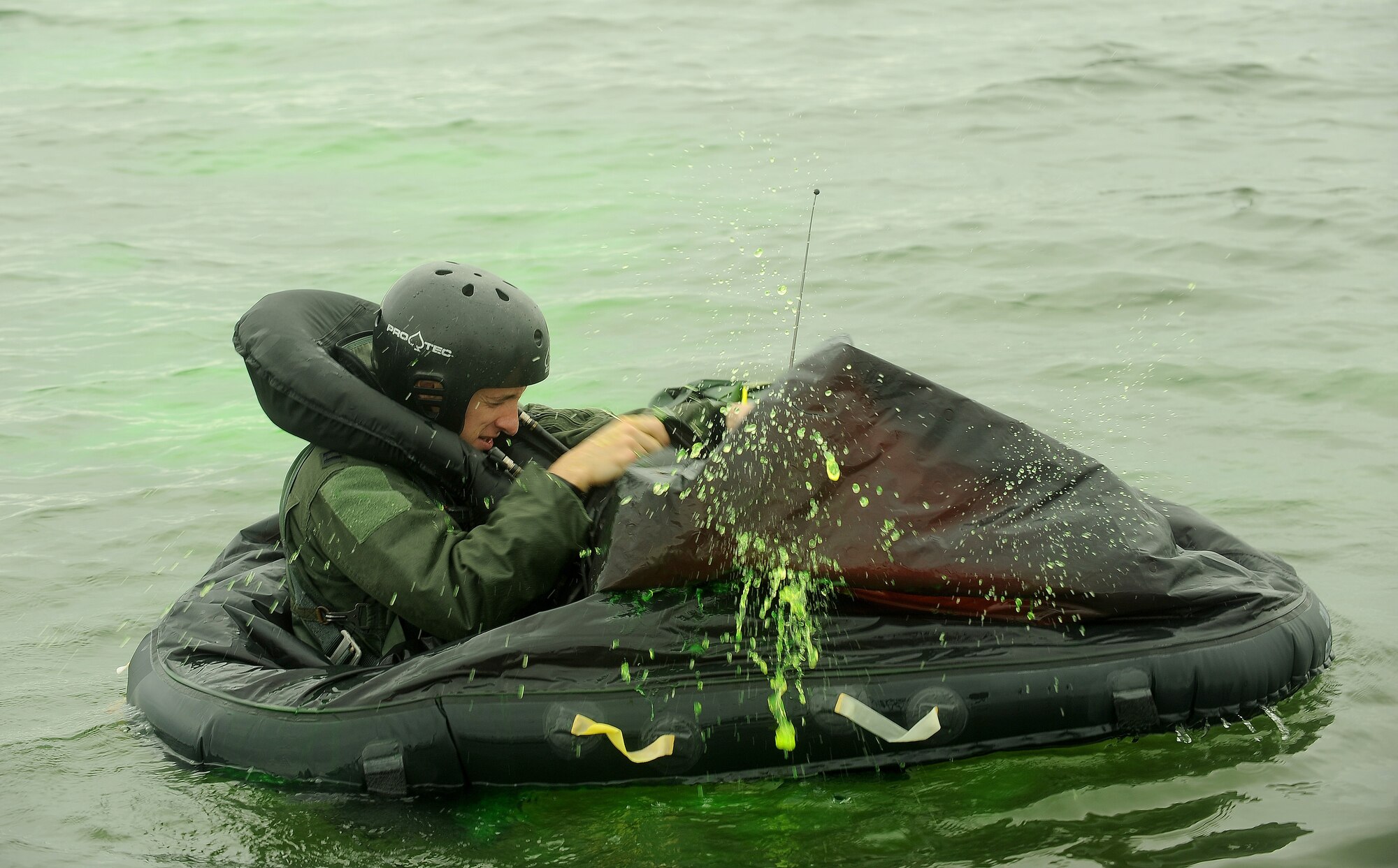 A fully uniformed service member removes water from his life raft in open water.
