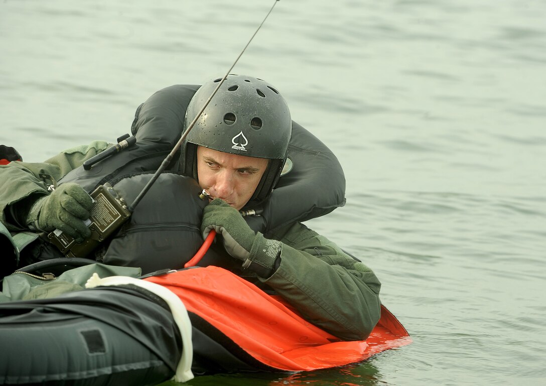 A fully uniformed man manually inflates a life raft in open water.
