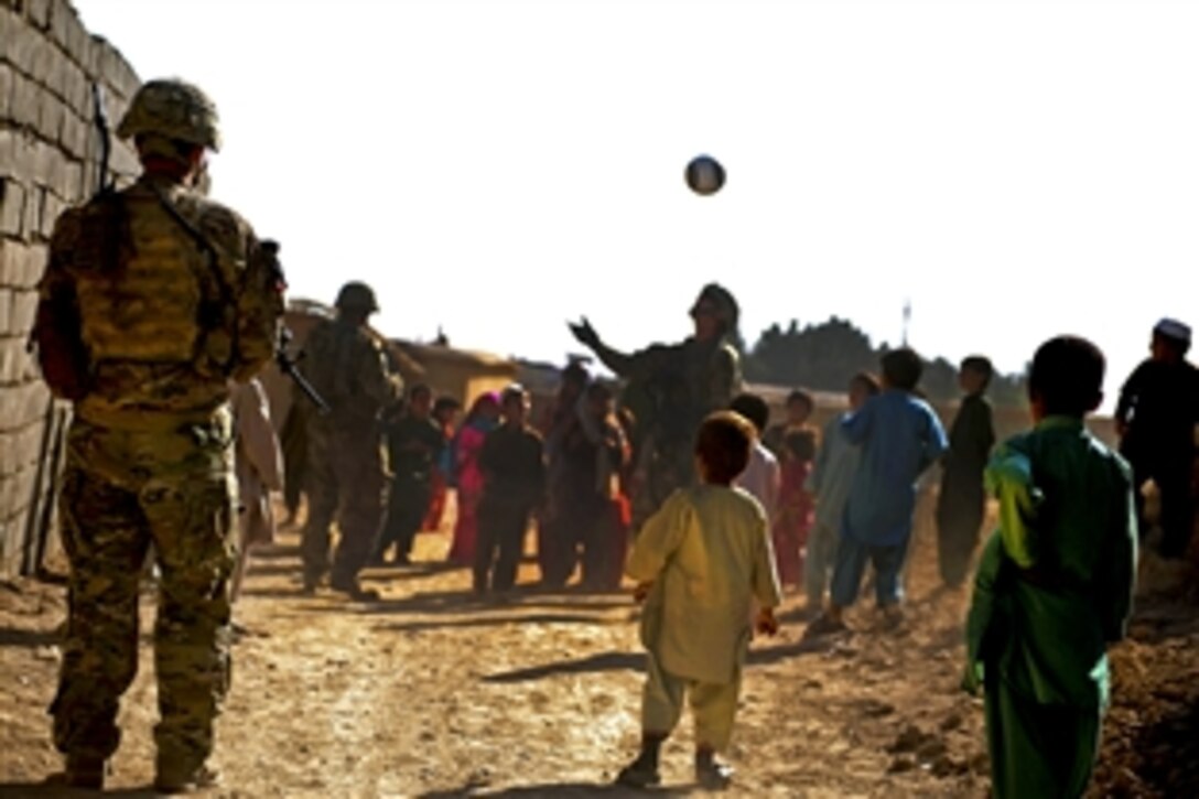 U.S. Army Sgt. Brandon Bregel, left, secures an area as Army Spc. Kevin Medeiros plays soccer with children during a foot patrol in Qalat City in Afghanistan's Zabul province, Sept. 25, 2011. Bregel, a team leader, and Medeiros, a rifleman, are members of Provincial Reconstruction Team Zabul and assigned tothe 182nd Division's Company C.