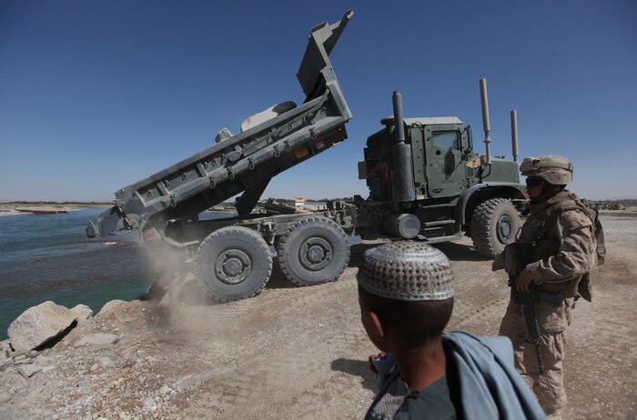 A local Afghan boy looks on as Marines with 7th Engineer Support Battalion, 2nd Marine Logistics Group (Forward), build a causeway near Forward Operating Base Sabit Qadam. Marines from different elements of 2nd MLG (FWD) are currently building patrol bases, combat outposts, and village stability platforms between Kajaki and Sangin in support of Operation Eastern Storm.