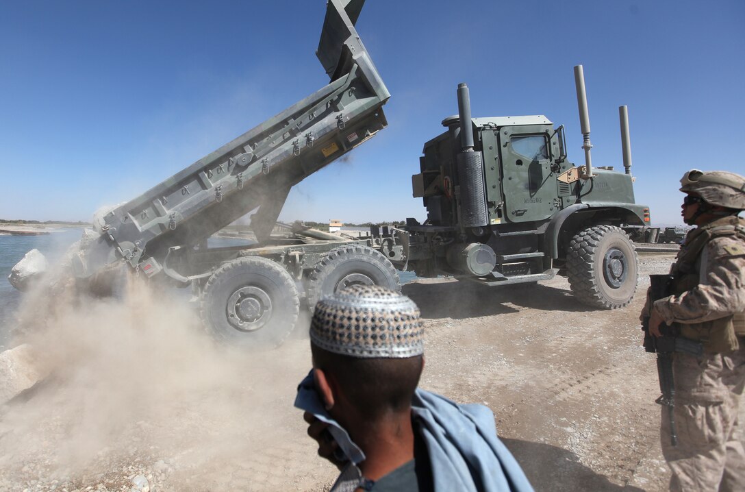 Seabees with Naval Mobile Construction Battalion 4 and Afghan locals watch as Marines with 7th Engineer Support Battalion 4 unload debris into Helmand River near Forward Operating Base Sabit Qadam, Afghanistan, Sept. 27. The concrete and stone mixture serves at the foundation of a causeway, which will provide a platform for a forthcoming bridge project. (U.S. Marine Corps photo by Sgt. Justin J. Shemanski)
