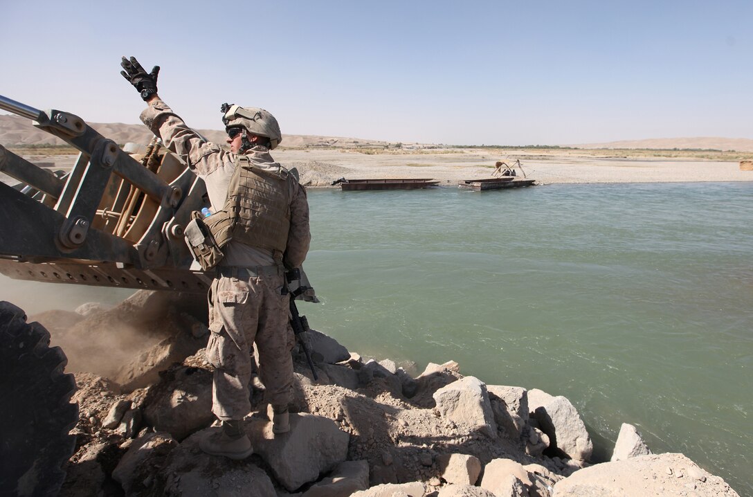 Cpl. Wade Hale, a heavy equipment operator with Support Company, 7th Engineer Support Battalion, directs the driver of a backhoe as newly-placed debris is pushed into place during a causeway construction project in Helmand River near Forward Operating Base Sabit Qadam, Afghanistan, Sept. 27. Marines have unloaded several metric tons of rock and concrete at the site which will eventually serve as a platform to launch a medium-girder bridge that will span the remainder of the river. (U.S. Marine Corps photo by Sgt. Justin J. Shemanski)