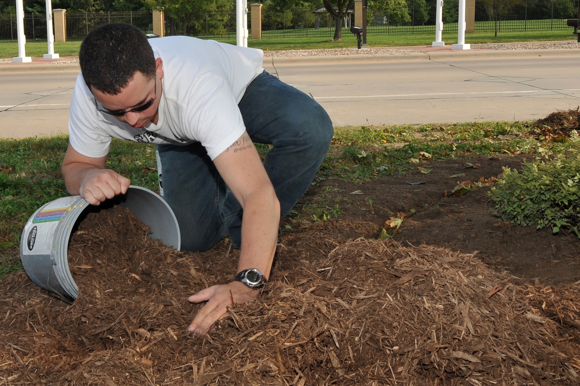 U.S. Air Force Senior Airman Ross Downing, 55th Medical Support Squadron, gathers mulch during a gate beautification project at the Kenney Gate on Offutt Air Force Base, Neb., Aug. 31. Team Offutt members and the Bellevue Garden Club came together to enhance the landscaping at the Kenney Gate. (U.S. Air Force photo by Charles Haymond/Released)