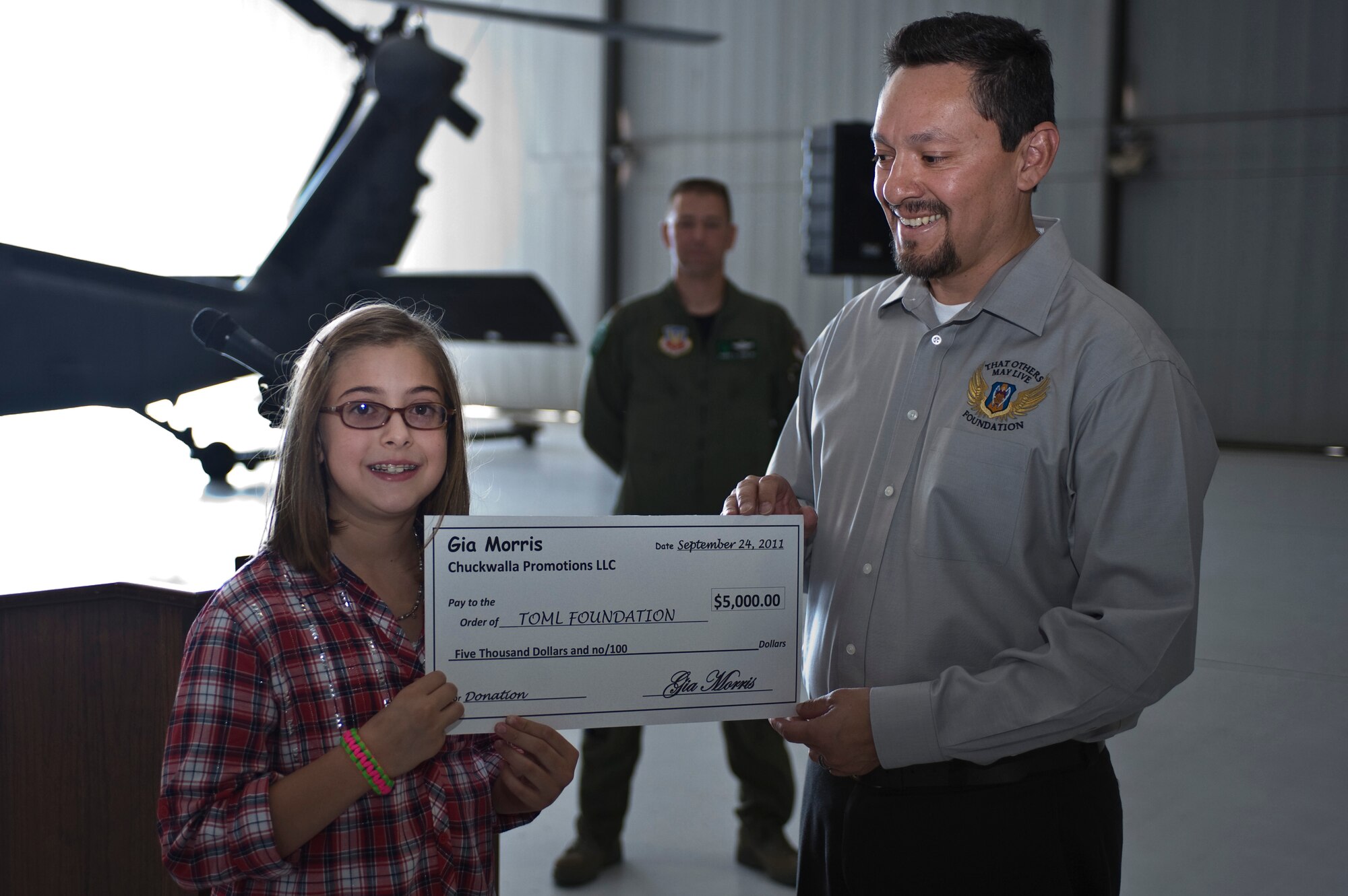 Gia Morris, 10, daughter of Steve Morris, presents a $5,000 donation to Robert Martinez, "That Others May Live" foundation executive member, Sept. 24, 2011, at Nellis Air Force Base, Nev. The TOML foundation is a non-profit charitable organization that provides scholarships, family counseling and aid to surviving children of United States Air Force rescue Airmen who gave the ultimate sacrifice during a rescue mission, training or other personnel recovery mission. (U.S. Air Force photo by Airman 1st Class Matthew Lancaster/Released)