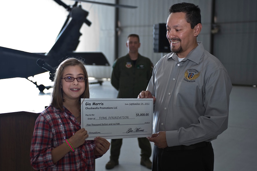 Gia Morris, 10, daughter of Steve Morris, presents a $5,000 donation to Robert Martinez, "That Others May Live" foundation executive member, Sept. 24, 2011, at Nellis Air Force Base, Nev. The TOML foundation is a non-profit charitable organization that provides scholarships, family counseling and aid to surviving children of United States Air Force rescue Airmen who gave the ultimate sacrifice during a rescue mission, training or other personnel recovery mission. (U.S. Air Force photo by Airman 1st Class Matthew Lancaster/Released)