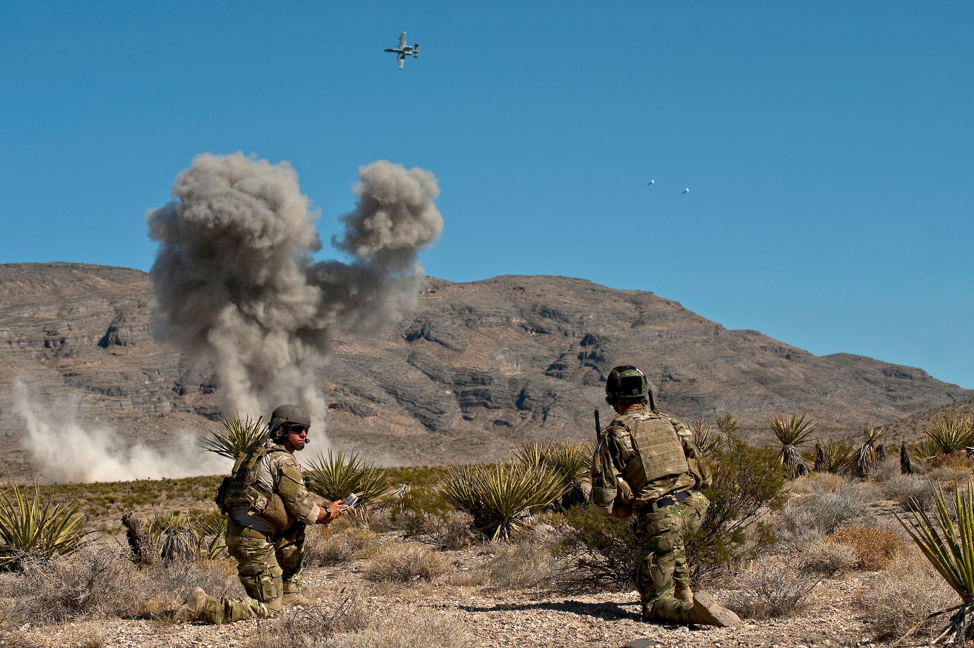 U.S. Air Force Senior Airman Corban Caliguire and Tech. Sgt. Aaron Switzer, 21st Special Tactics Squadron joint terminal attack controllers, from Pope Field, N.C., look on as an A-10 Thunderbolt II releases its munitions during a close air support training mission Sept. 23, 2011, at the Nevada Test and Training Range.  Joint Terminal Attack Controllers perform proficiency training with U.S. Air Force Weapons School students during the close air support phases of the Weapons School six-month, graduate-level instructor course. (U.S. Air Force photo by Tech. Sgt. Michael R. Holzworth/Released)