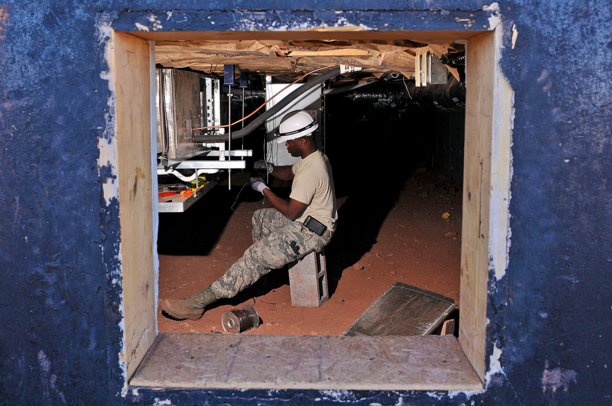 Senior Airman Travis Shelley, 116th Civil Engineering Squadron, Robins Air Force Base, Ga., runs wiring for a thermostat on a new HVAC system in the crawl space under the new adult life skills center at St. Michaels Association for Special Education, Window Rock, Ariz., June 8, 2011.  Shelley and more than 40 members of his squadron deployed to the Navajo Nation as a part of the Department of Defense Innovative Readiness Training program. (U.S. Air Force photo by Master Sgt. Roger Parsons/Released)