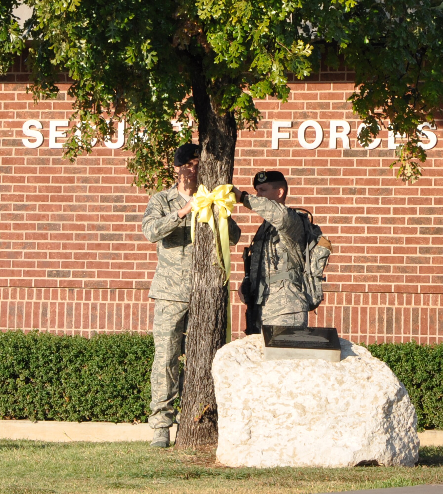 GOODFELLOW AIR FORCE BASE, Texas – (From left:) Tech. Sgt. Russell Weatherby, 17th Security Forces Squadron, and Maj. Dennis Turriff, 17th SFS Commander, tie a yellow ribbon around a tree at the security forces building Sept. 28 in remembrance of fellow security forces member Airman 1st Class Elizabeth Jacobson.  Jacobson was the first security forces member and the first Air Force female to be killed in action in Operation Iraqi Freedom, Sept. 28, 2005, by a roadside bomb. (U.S. Air Force photo/Connie Hempel)