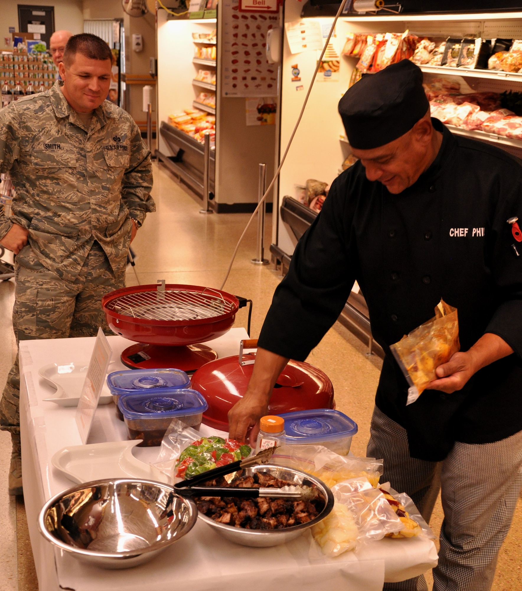 Chef Phil Barfield prepares free beef shish kebabs Sept. 27 on Grand Forks Air Force Base as Tech. Sgt. Stephen Smith, Area Defense Counsel, looks on.  The GFAFB Commissary hosted the cooking exhibition in support of DeCA initiative “Go Lean with Protein.” (U.S. Air Force photo/Airman 1st Class Derek VanHorn)