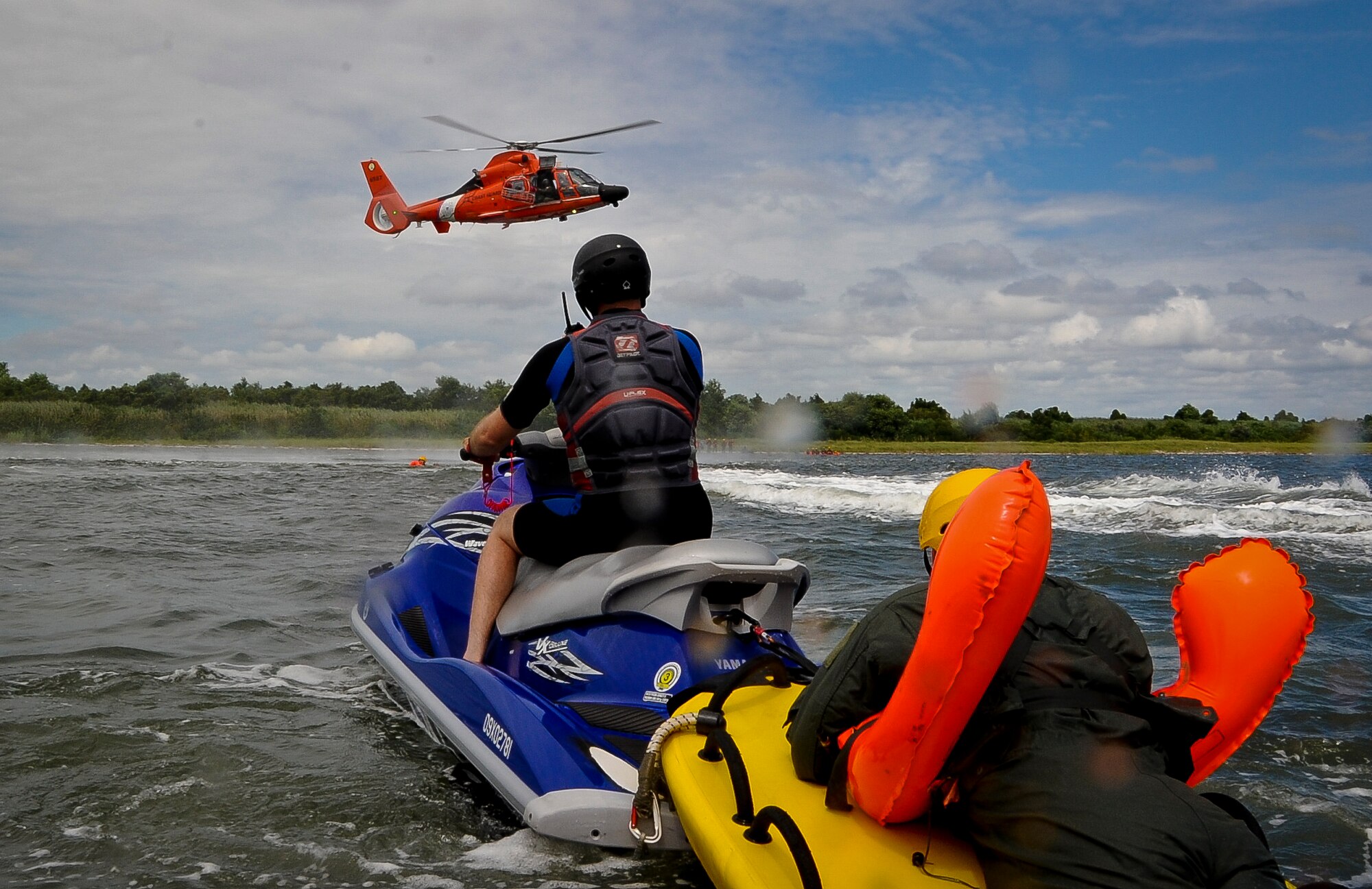 Staff Sgt. Timothy Giordana, Joint Base McGuire-Dix-Lakehurst Survival Evasion Resistance and Escape instructor, watches Coastguardsmen from Coast Guard Air Station Atlantic City, N.J. simulate a water rescue mission with JB MDL air crew members Aug. 4 at Barnegat Bay, N.J. Giordana used a jet ski to position the air crew members in the water so a Coast Guard rescue swimmer could guide them into a basket attached to an H-65 Dolphin rescue helicopter. (U.S. Air Force photo by Airman 1st Class Dennis Sloan/Released)