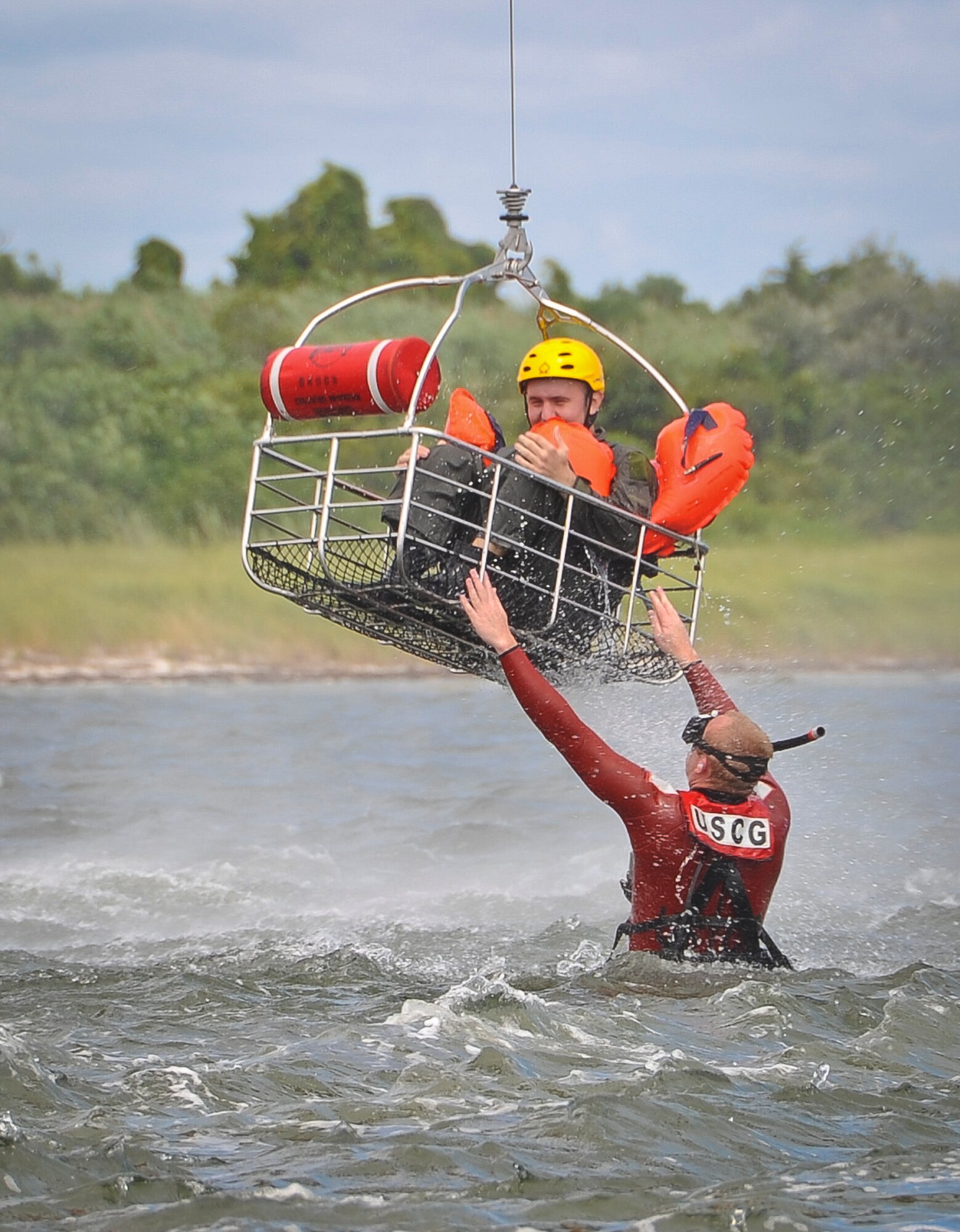 A Coast Guard rescue swimmer from Coast Guard Air Station Atlantic City, N.J. stabilizes a rescue basket, which holds a Joint Base McGuire-Dix-Lakehurst air crew member, as it is hoisted up by an H-65 Dolphin rescue helicopter Aug. 4 at Barnegat Bay, N.J. More than 15 Airmen were hoisted from the water with the help of a Coast Guard rescue swimmer. Staff Sgt. Andrew Dunn and Staff Sgt. Timothy Giordana, JB MDL Survival Evasion Resistance and Escape instructors, trained JB MDL air crew members on several water survival techniques to include: entering and exiting a survival raft, properly wearing a cold water survival suit and staying warm in cold water situations. (U.S. Air Force photo by Airman 1st Class Dennis Sloan/Released)