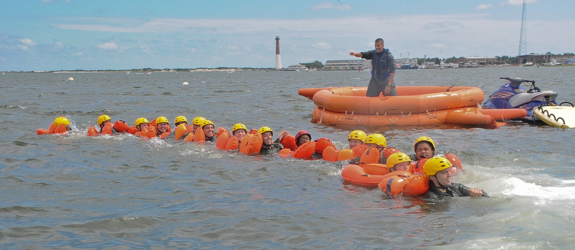 Staff Sgt. Andrew Dunn, Joint Base McGuire-Dix-Lakehurst Survival Evasion Resistance and Escape instructor, directs JB MDL air crew members to form a human chain during water survival training Aug. 4 at Barnegat Bay, N.J. The crew members were trained on how to properly wear their cold water survival suits as well as how to properly enter and exit a survival raft. Coastguardsmen from Coast Guard Air Station Atlantic City, N.J., simulated a rescue situation by using H-65 Dolphin rescue helicopter equipped with a basket to hoist them out of the water. (U.S. Air Force photo by Airman 1st Class Dennis Sloan/Released)