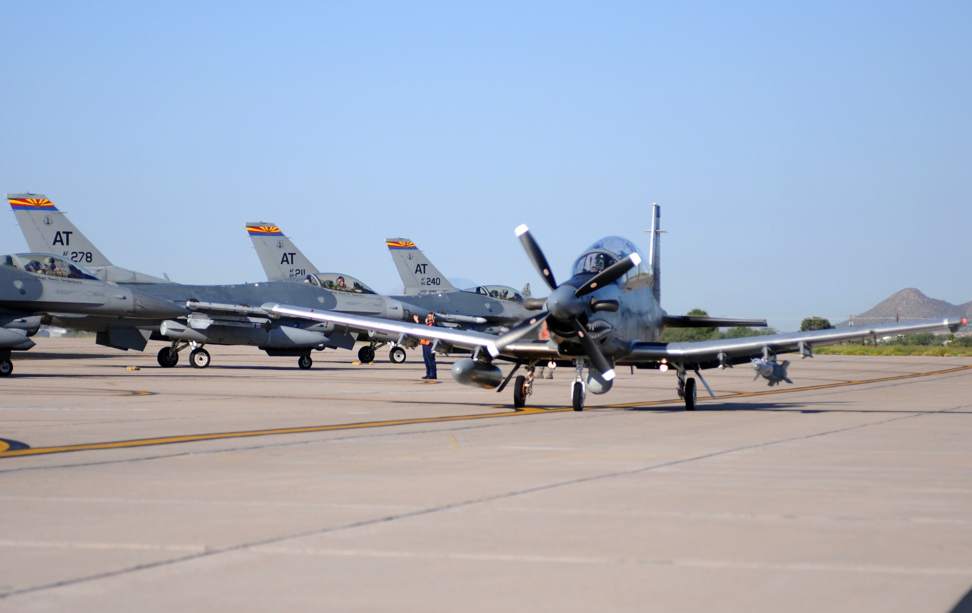 An AT-6C light attack aircraft taxis by F-16s at Tucson International Airport Sept. 28 on its way to the Barry M. Goldwater Range to drop the first precision munition ever employed on the experimental aircraft. (U.S. Air Force photo/Maj. Gabe Johnson)
