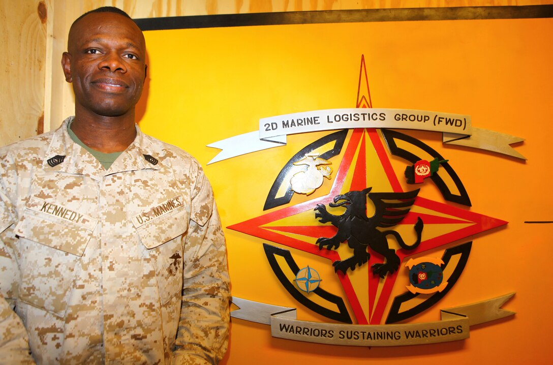 Master Sgt. Mark Kennedy, an administration chief with 2nd Marine Logistics Group (Forward) stands next to his unit logo in his office building aboard Camp Leatherneck, Afghanistan, Sept. 20, 2011.  Kennedy recently sang the national anthem at the 9/11 memorial ceremony and is involved with the gospel choir at the base chapel.  (U.S. Marine Corps photo by Cpl. Katherine M. Solano)