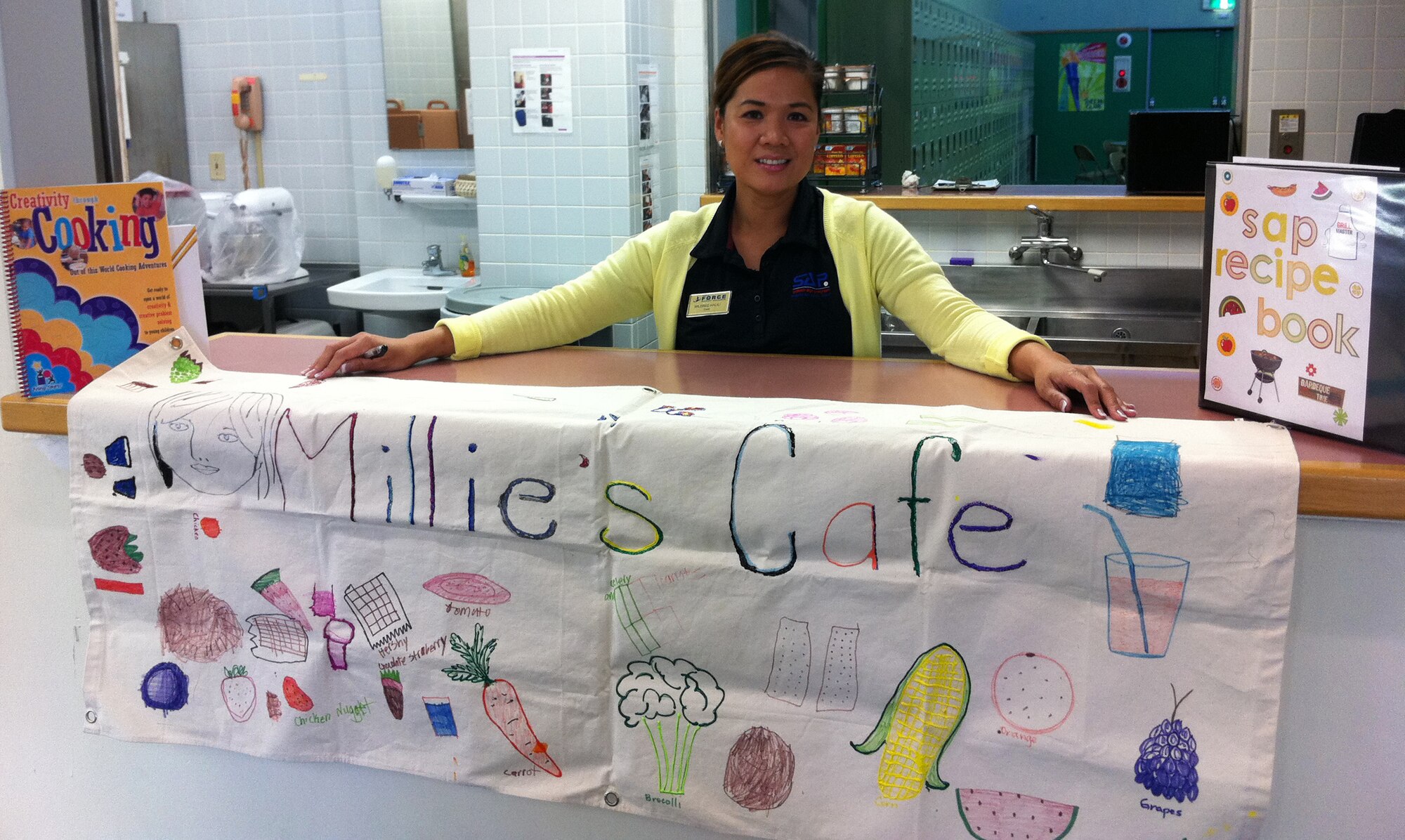 YOKOTA AIR BASE, Japan -- Mildred Halili holds her kitchen's banner outside her kitchen at the School Age Program building June 24, 2011, at Yokota Air Base, Japan. In her first year of working at Yokota, Halili put her skills to the test in a Pacific Air Force-wide competition and won. (U.S. Air Force photo/Airman John D. Partlow)