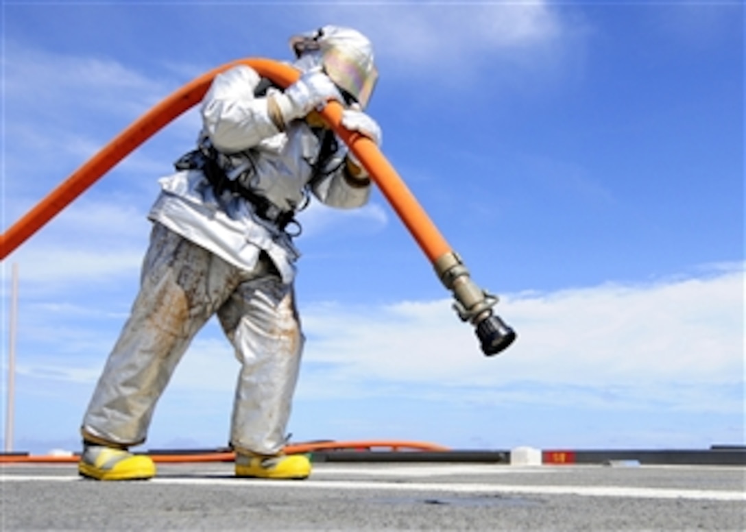 U.S. Navy Petty Officer 2nd Class Joshua B. Cary carries a charged fire hose across the flight deck of the amphibious transport dock ship USS Denver (LPD 9) during crash and salvage endurance training while the ship operates in the East China Sea on Sept. 27, 2011.  Cary is a Navy aviation support equipment technician.  