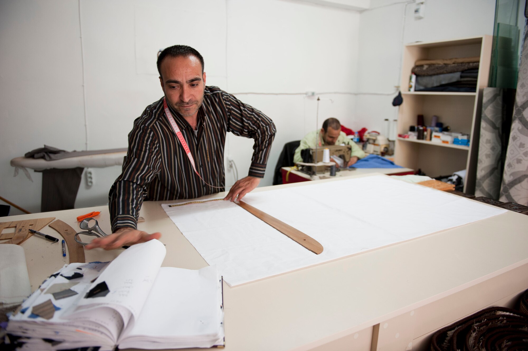 Mehmet Menter measures cloth, while Veysel Arsay operates a sewing machine, March 29, 2012, in Incirlik Village, Turkey. Menter and Arsay are employed by Couzin's Tailor Shop, a member of the Incirlik Village Merchants Association, and spent 19 and seven years, respectively, working in Incirlik Village. (U.S. Air Force photo by Senior Airman Clayton Lenhardt/Released)