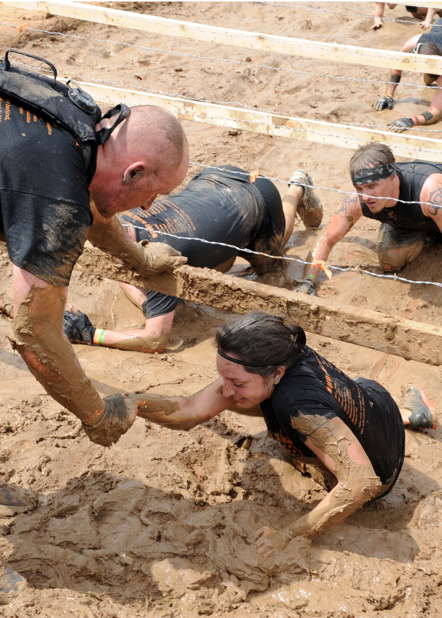U.S. Air Force 1st Lt. Carl Bemis, left, helps Senior Airman Pauline Guerrero, 7th Medical Operations Squadron, from underneath the “Kiss of Mud” obstacle at the Dallas Tough Mudder event March 31, 2012 in Wortham, Texas. Tough Mudder events are 10-12 mile runs with obstacles designed by British Special Forces to test all around strength, stamina, mental grit and camaraderie. To date, Tough Mudder has raised more than $2,886,000 for the Wounded Warrior Project to aid and assist wounded service members. For more information on locations and events visit http://www.toughmudder.com (U.S. Air Force photo by Airman 1st Class Peter Thompson/Released)