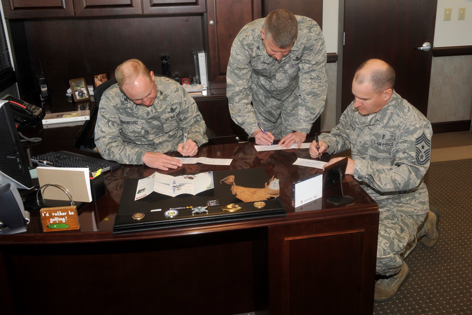 PETERSON AIR FORCE BASE, Colo. - (Left to right) Col. Chris Crawford, 21st Space Wing commander, Col. Jeffrey Flewelling, 21st SW vice commander, and Chief Master Sgt. Thomas Trottier, 21st SW command chief master sergeant, sign their Air Force Assistance Fund forms March 27 in Crawford’s office. The campaign runs through May 4 and donations benefit one of four Air Force charities: the Air Force Aid Society, Air Force Village, Air Force Enlisted Village, or the Gen. and Mrs. Curtis E. LeMay Foundation. (U.S. Air Force photo/Robb Lingley)
