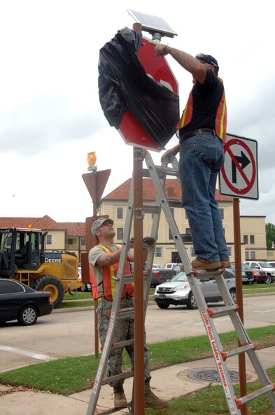 Staff Sgt. Davin Stege, 2nd Civil Engineer Squadron, stabilizes the ladder for Jerry Jacobson, 2 CES, on Barksdale Air Force Base, La., April 3. Stege and Jacobson installed a solar panel on the newly placed stop signs on the intersection of Davis Avenue West and Barksdale Boulevard West. (U.S. Air Force photo/Airman 1st Class Joseph A. Pagán Jr.)(RELEASED)