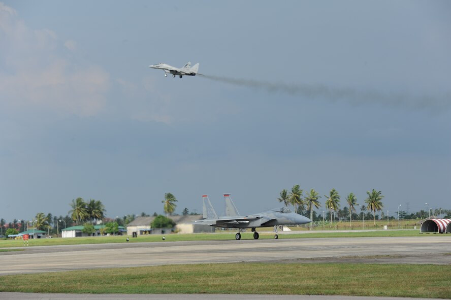 A Royal Malaysian Air Force MiG-29N Fulcrum makes a pass over the airfield while an F-15C from the 67th Fighter Squadron at Kadena Air Base, Japan, taxis during the first full day of flying in Cope Taufan 2012 at TUDM Butterworth in northwestern Malaysia Apr. 4, 2012. Cope Taufan, the biennial live-flying exercise between the U.S. Air Force and RMAF, includes dissimilar basic fighter maneuvers and dissimilar air combat tactics training. (U.S. Air Force photo/Master Sgt. Matt Summers/released)