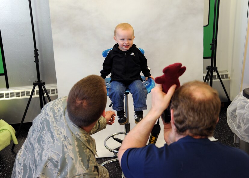 Staff Sgt. Aaron Mills, left, and a photographer entertain 1-year-old Landon Mills before taking his picture during the Beautiful Child Photo Shoot and Activity Fair on Grand Forks Air Force Base, N.D, on April 3, 2012.