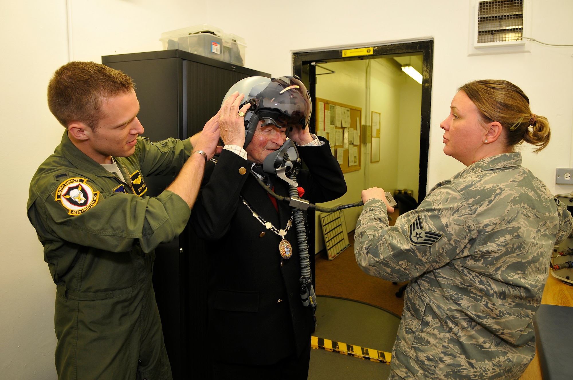 ROYAL AIR FORCE LAKENHEATH, England -- 1st Lt. David Kuhn, left, 493rd Fighter Squadron pilot, and Staff Sgt. Jessica Jackson, right, 493rd FS aircrew flight equipment craftsman, help The Worshipful The Mayor of St. Edmundsbury, Councillor Christopher Spicer, try on a Joint Helmet Mount Cueing System during his tour through the 493rd FS April 2, 2012.  Councillor Spicer toured the 493rd FS facilities to learn more about the history of the unit, to meet with the Airmen and to try on equipment from the life support section.  (U.S. Air Force photo by Staff Sgt. Connor Estes)