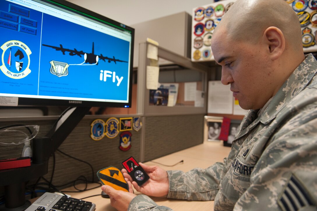 Air Force Staff Sgt. Jose Castillo reflects his inspiration for creating his "iFly" program at his desk March 28 in the 537th Airlift Squadron, Joint Base Elmendorf-Richardson, Alaska. The patch in his left hand was a gift from his grandfather, who served in Vietnam and continues to inspire Castillo's career. The patch in his right hand comes from a training course for pilots that gave him the name "iFly.? The wall of patches behind him has been collected throughout his career and, for him, represent his commitment to his job. Castillo serves as the aviation resource management noncommissioned officer in charge. While serving there, he created "iFly," which tracks training for pilots. (U.S. Air Force photo/Staff Sgt. Robert Barnett)