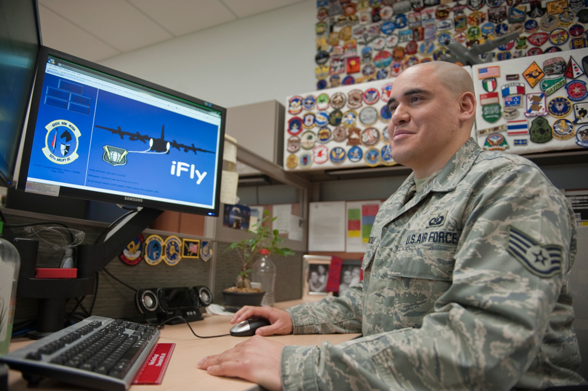 Air Force Staff Sgt. Jose Castillo works in his "iFly" program March 28 in the 537th Airlift Squadron, Joint Base Elmendorf-Richardson, Alaska. The wall of patches behind him has been collected throughout his career and, for him, represent his commitment to his job. Castillo serves as the aviation resource management noncommissioned officer in charge. While serving there, he created "iFly,? which tracks training for pilots. (U.S. Air Force photo/Staff Sgt. Robert Barnett)