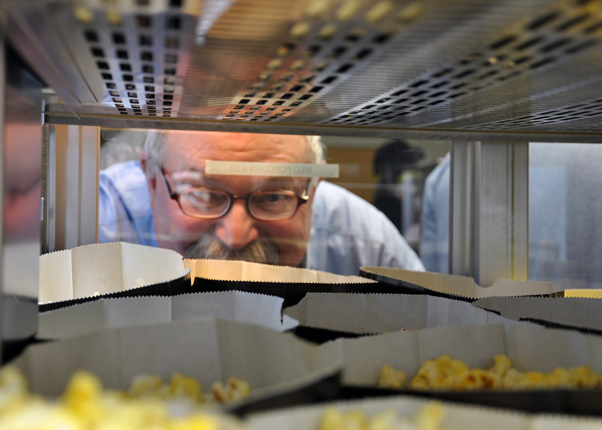 SPANGDAHLEM AIR BASE, Germany – Wayne Phillips, Cubic aircraft simulator manager and moviegoer, examines bags of popcorn at the “Reel Time Express” snack bar in the Spangdahlem Skyline Theater here April 4 after the theater’s reopening ceremony. The military Exchange contributed $350,000 to upgrade the facility’s systems, to include a newer self-service snack bar. The total cost for the project was $925,850, making this the first Exchange theater in the world to have 3-D capabilities and full digital audio and video. (U.S. Air Force photo by Staff Sgt. Daryl Knee/Released)