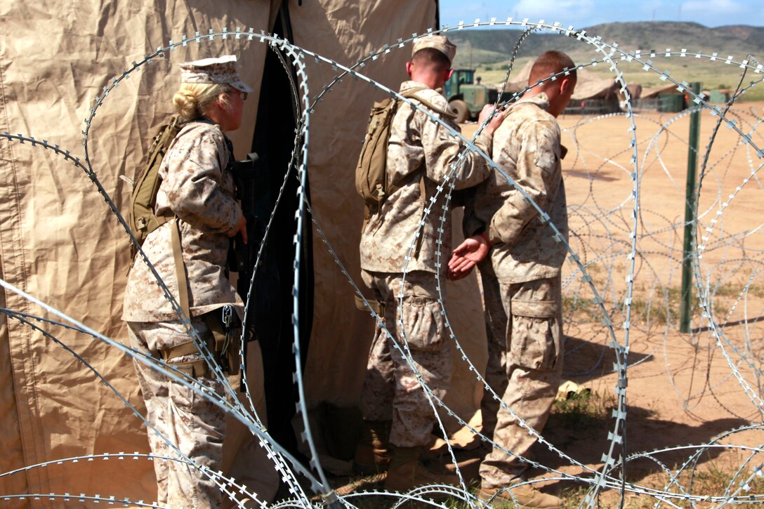 Lance Cpls. Sidney B. Ward and Alecia R. Mesch, field military police, MP Detachment, Combat Logistics Battalion 15, 15th Marine Expeditionary Unit, escort Lance Cpl. William E. Curry, a simulated detainee, into the processing facility of the detention center they built as a part of MP training during MEU Exercise, here, April 5. The construction of the facility took the Marines an entire day. It includes two large working tents, two large metal storage containers and six pallets of concertina wire, all for a training facility half the size of one they would build if called to shore. Curry, 20, is a native of Philadelphia. Ward, 20, is a native of Dardonelle, Ark. Mesch, 20, is a native of Denver. They are all field MPs with the MP detachment, Combat Logistics Battalion 15, 15th MEU.