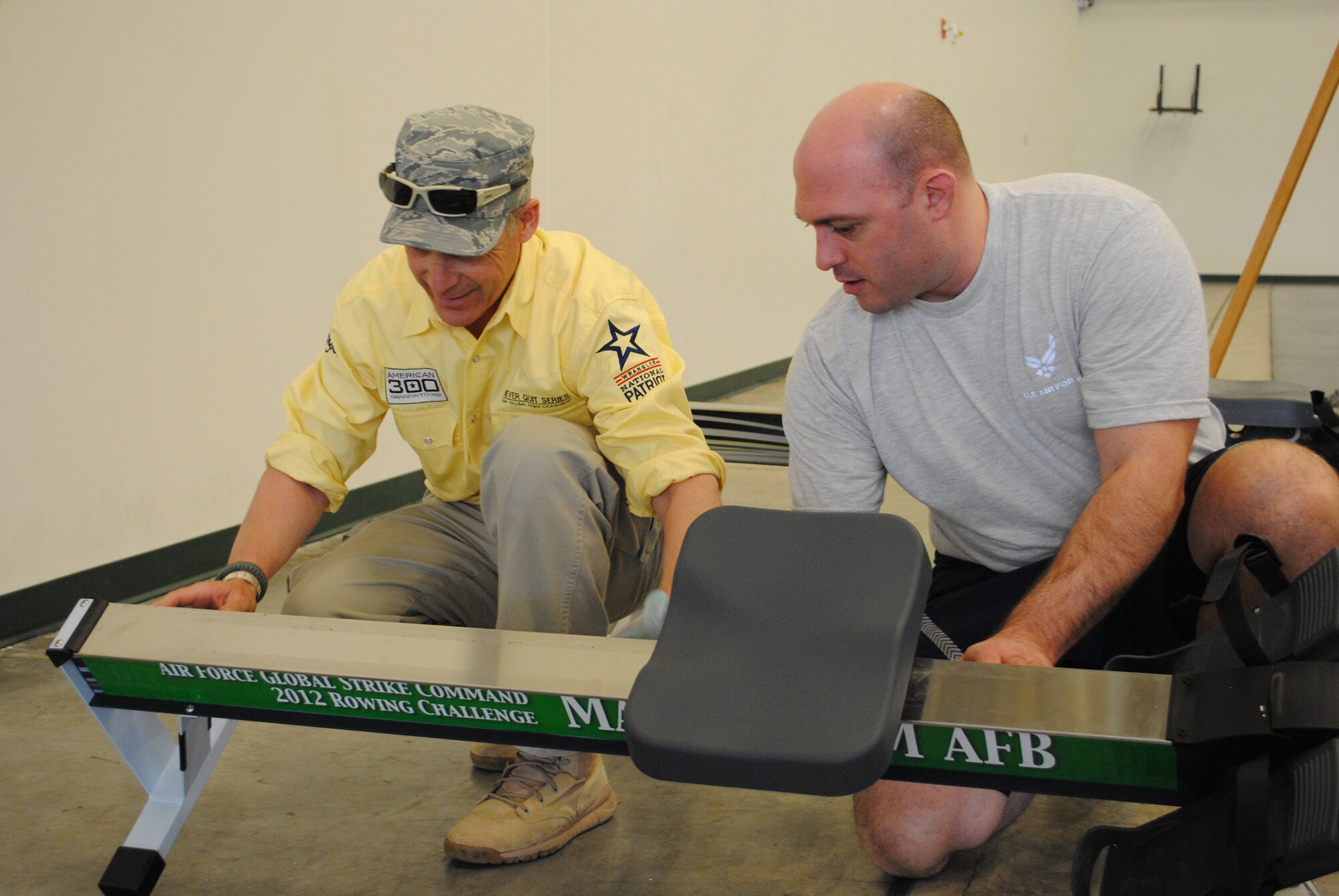 Robi Powers, founder of the American300 Warrior Tours, positions a green Malmstrom Air Force Base sticker on the side of a rowing machine with help from Staff Sgt. William McKowan, OL AK, before beginning a rowing demonstration April 3 at the fitness center.  The green stickers mark Malmstrom's official rowing machine for the Air Force Global Strike Command rowing competition, which started April 5 and will run through May 5.  (U.S. Air Force photo/Airman 1st Class Cortney Paxton)