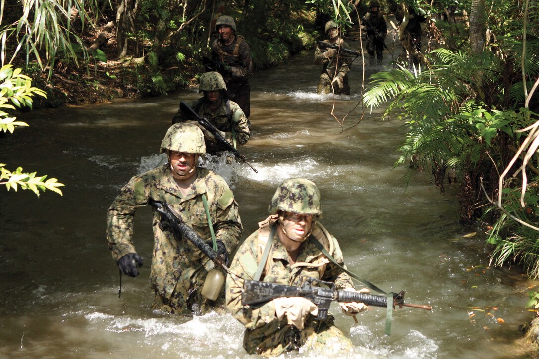 Marines and sailors run through a stream at the endurance course at the Jungle Warfare Training Center on Camp Gonsalves April 8. The 3.8-mile endurance course consists of 10 hasty rappelling obstacles, two water obstacles, a pit and pond, a stretcher carry, a commando crawl and a monkey crawl. The Marines and sailors are with Combat Logistics Regiment 37, 3rd Marine Logistics Group, III Marine Expeditionary Force, and Naval Mobile Construction Battalion 40, 31st Seabee Readiness Group.
