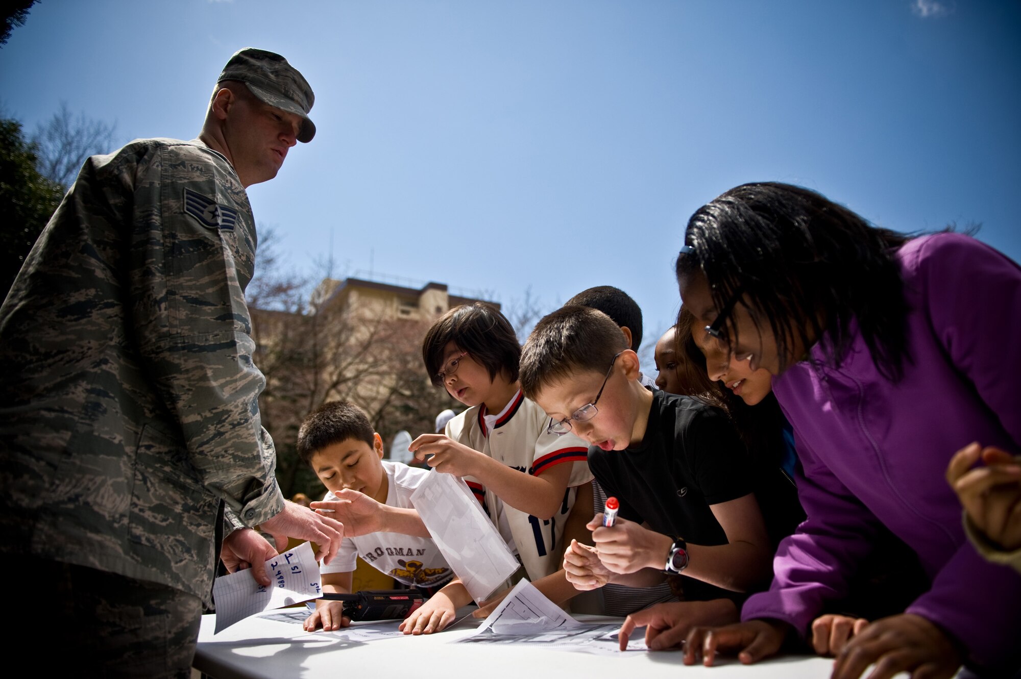 YOKOTA AIR BASE, Japan -- Staff Sgt. Corey Tharp, 374th Civil Engineer Squadron firefighter crew chief, watches as 5th grade students from Joan K. Mendel Elementary School solve math problems as part of an amazing race competition during Science, Technology, Engineering and Math Week at Yokota Air Base, Japan, Apr. 4, 2012.  Students participated in various activities involving science, engineering and math. (U.S. Air Force photo/Airman 1st Class Krystal M. Garrett)