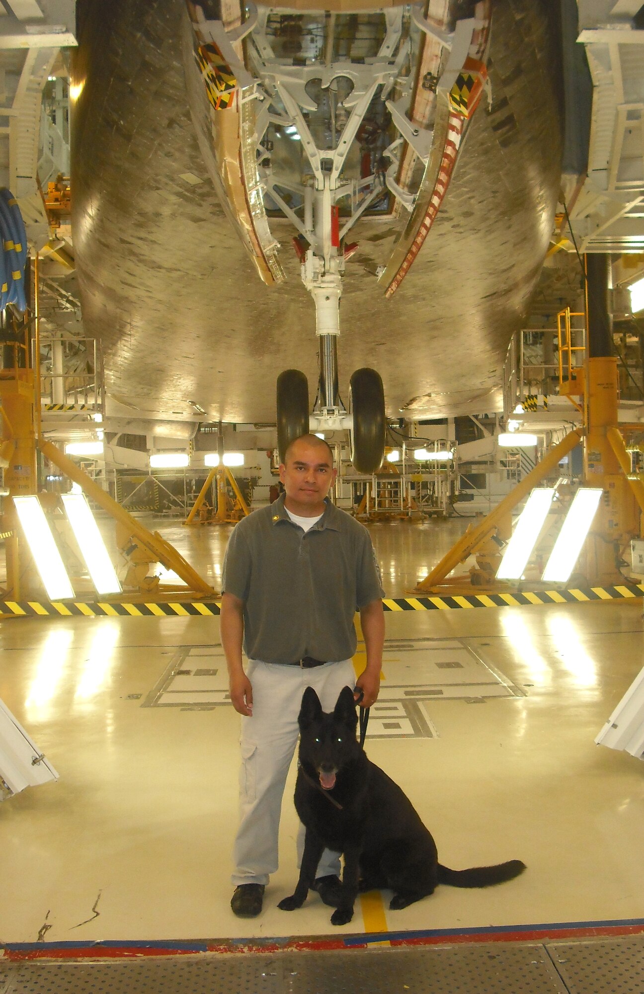 Staff Sgt. Juventino Salazar and his military working dog, Cini, pose near a space shuttle during a security detail for President Barack Obama’s visit to Cape Canaveral, Fla., for a space shuttle launch last summer. Cini died in Salazar’s arms March 22 on the door step of the kennel at Vance Air Force Base, Okla. (Courtesy photo)