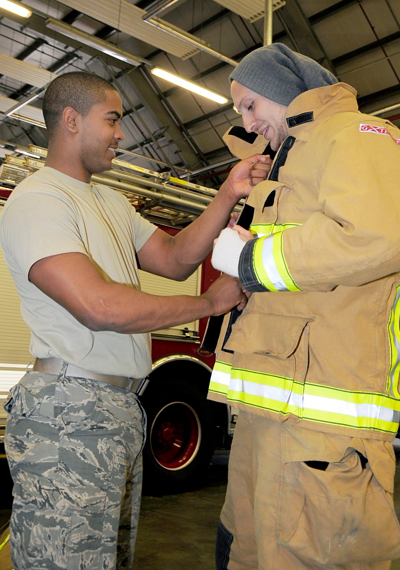 RAF MILDENHALL, England -- Airman 1st Class Theodore Willis, 100th Civil Engineer Squadron firefighter, assists Jon Hill, Teenage Cancer Trust member, with putting on firefighter structural gear during a tour of the fire department for the TCT here April 4, 2012. TCT members put on the firefighter gear to gain a better understanding of what firefighters have to wear when battling fires. (U.S. Air Force photo/Senior Airman Ethan Morgan)